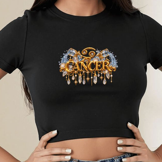 A woman wearing a black short-sleeve crop top with a gold and blue 'CANCER' graphic on the chest, paired with a blue denim skirt in a bright indoor setting.
