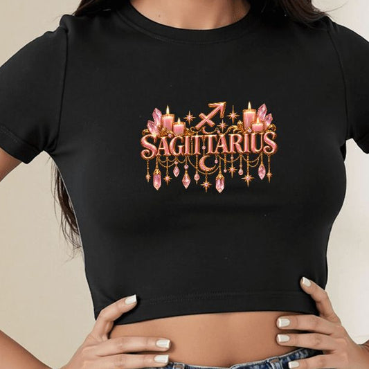A woman wearing a fitted black crop top T-shirt with a gold chandelier and 'LEO' graphic on the chest, paired with a blue denim skirt in a brightly lit indoor room.